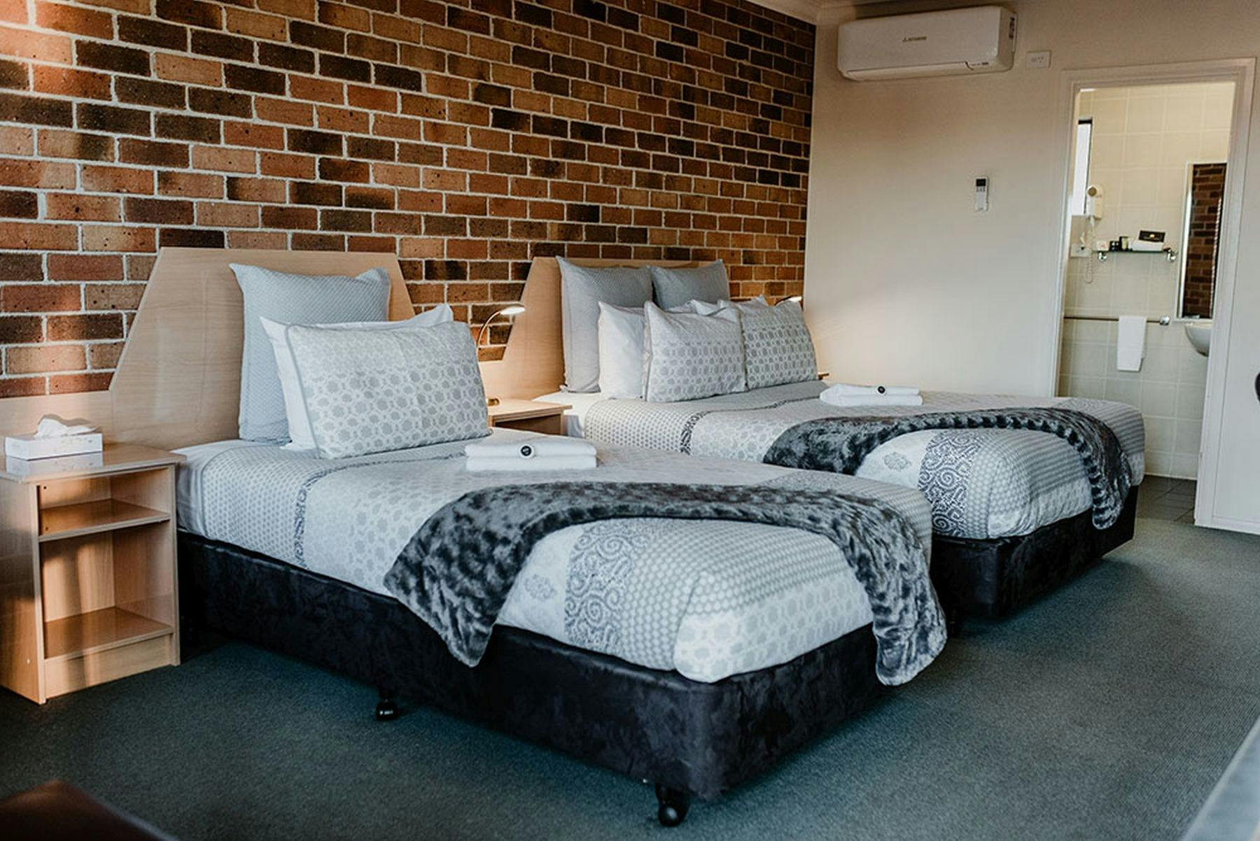 レンガの壁の左側にシングルベッド 1 台とクイーンベッド 1 台、背景にバスルームへの入り口