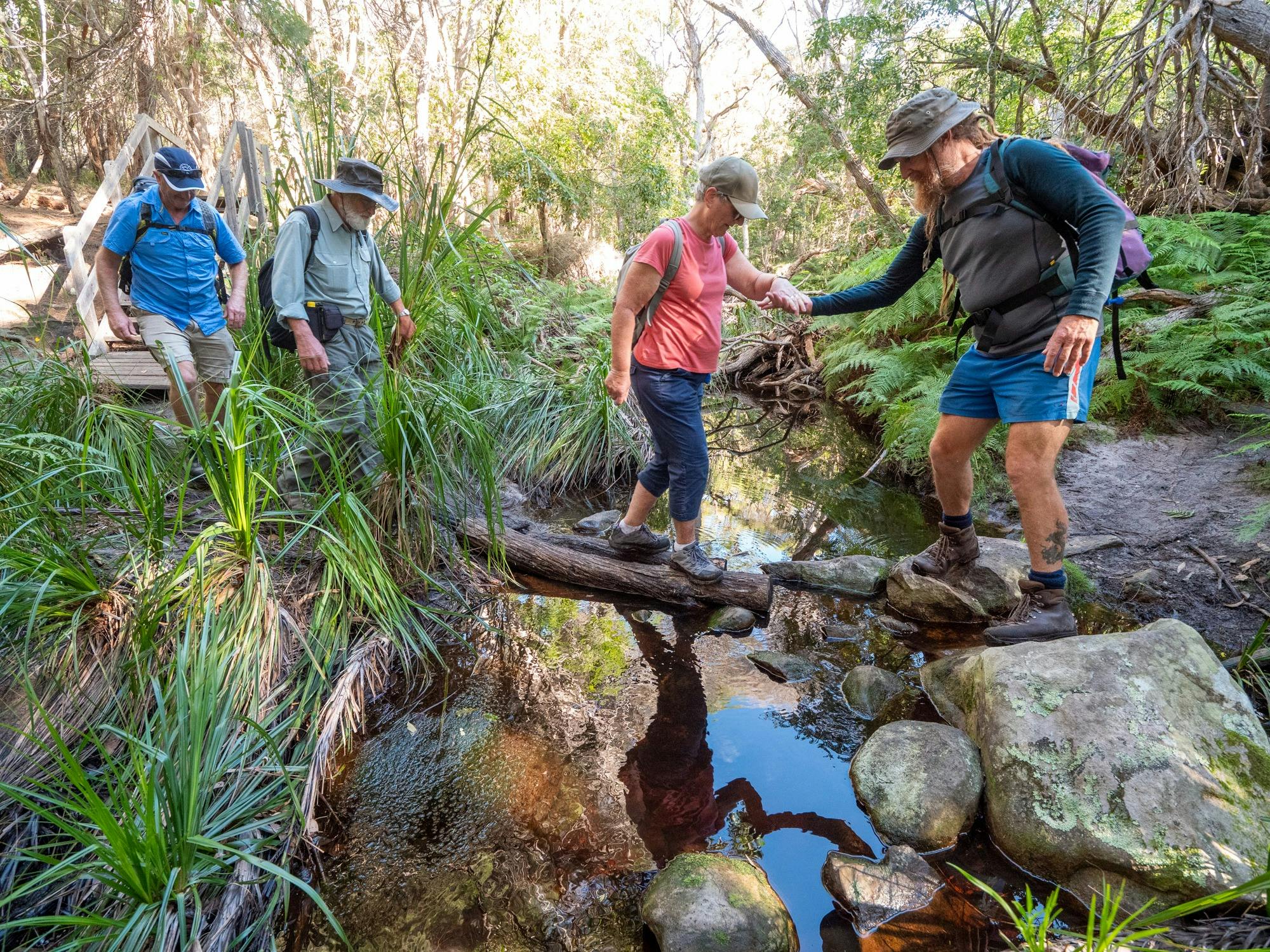 A guide reaching out to help a guest cross a stream