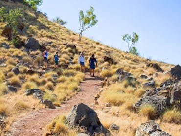 Four people walking on dirt track on grassy slope with rocky outcrops Four people walking on dirt track on grassy slope with rocky outcrops