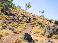 Four people walking on dirt track on grassy slope with rocky outcrops