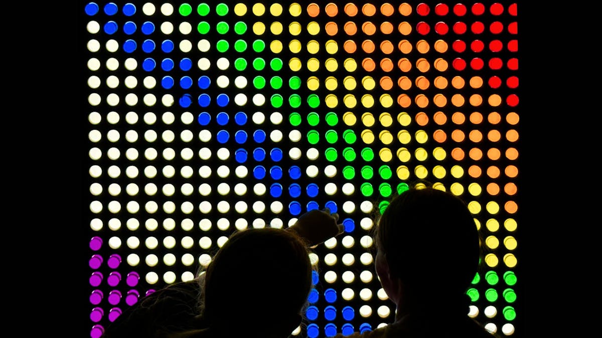 A photograph of children creating a colourful design on a large lightbox