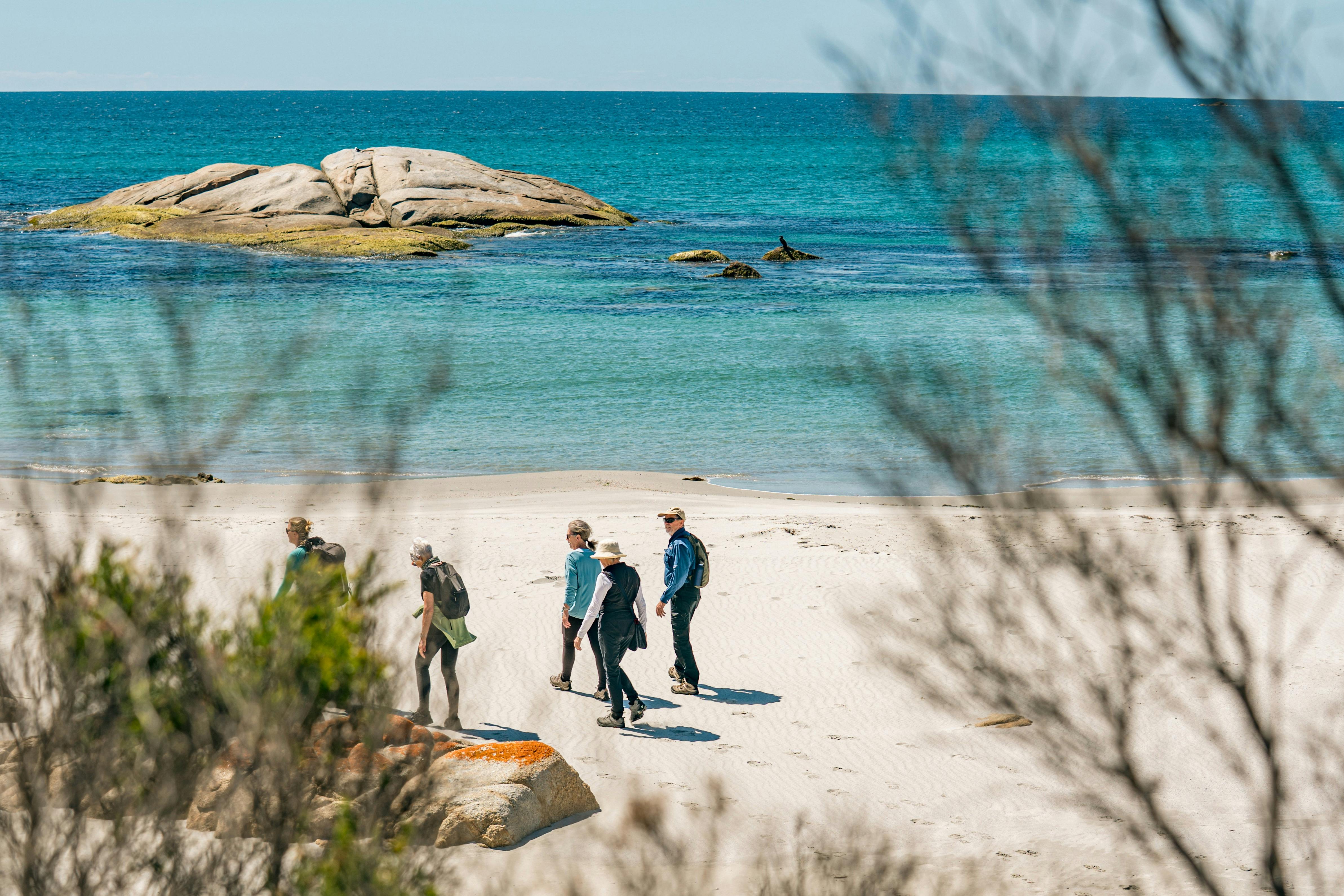 Group of walkers on a white sand beach with bright blue water in the back ground on a sunny day