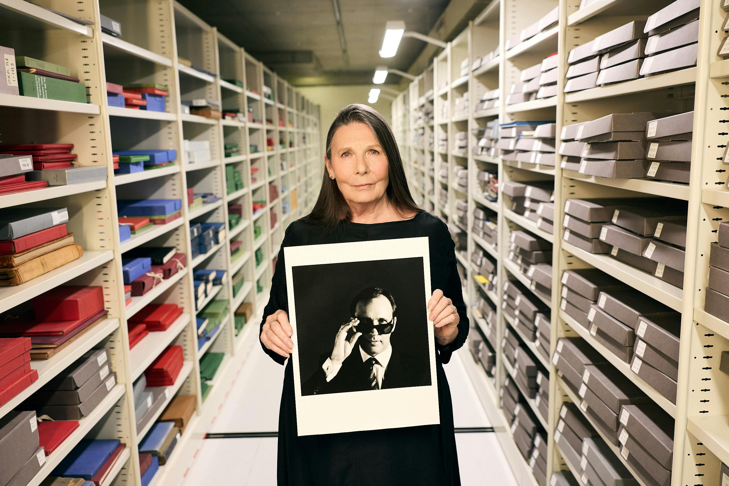 A woman standing in an archive holding a black and white photograph