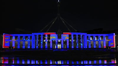 Parliament House at night, illuminated in blue & red light with projected artwork across the façade