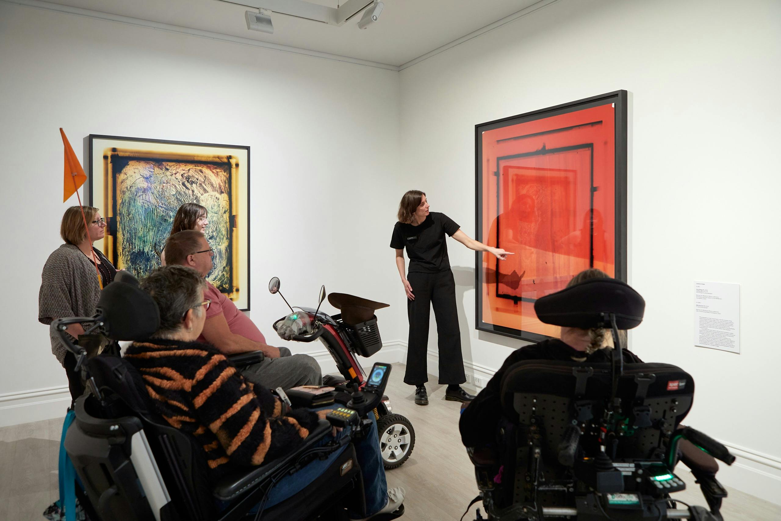 A group of wheelchair users and other adults enjoy a talk in front of large scale photographs