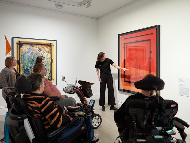 A group of wheelchair users and other adults enjoy a talk in front of large scale photographs