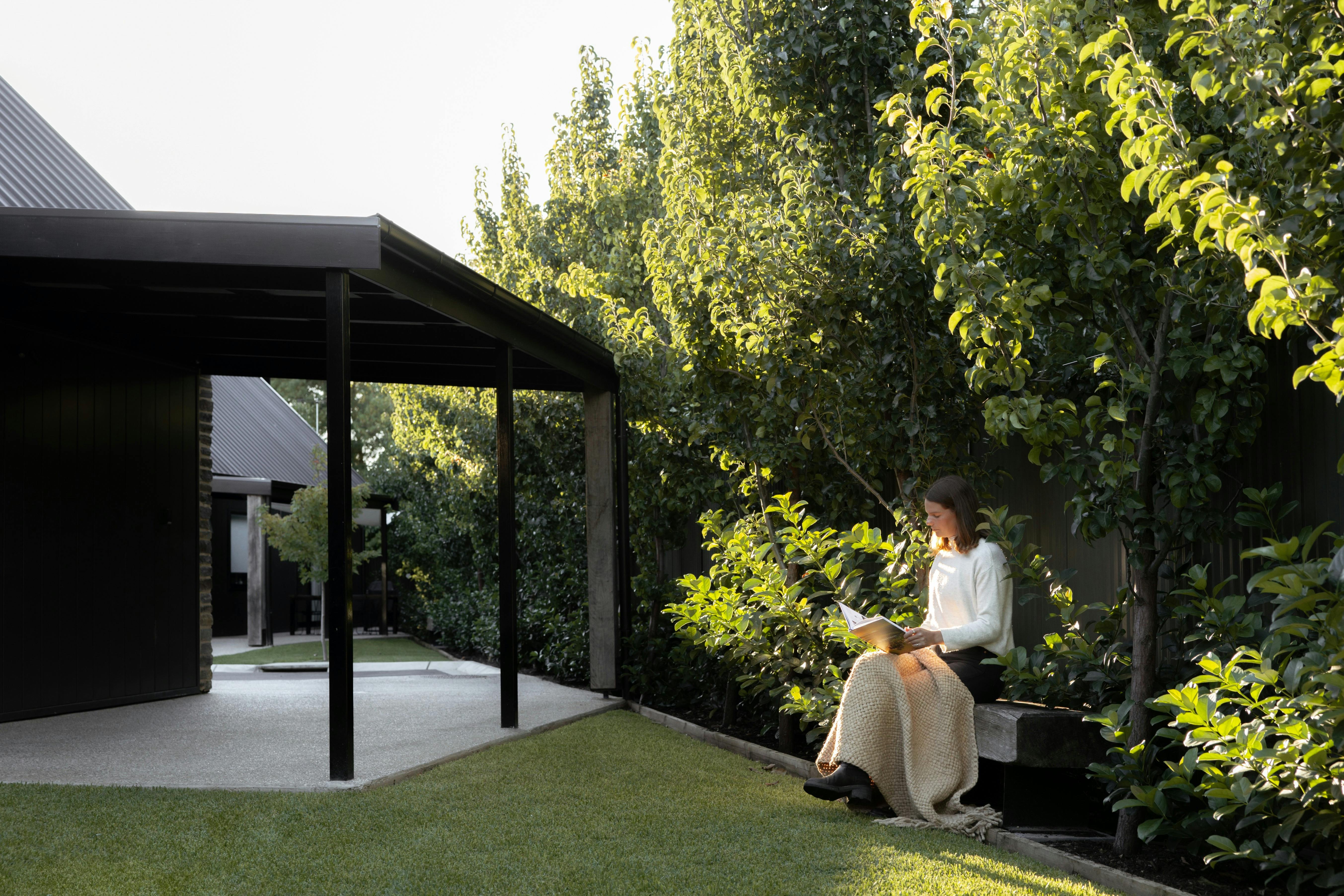 Woman in a garden sitting on a bench with trees glowing behind her.