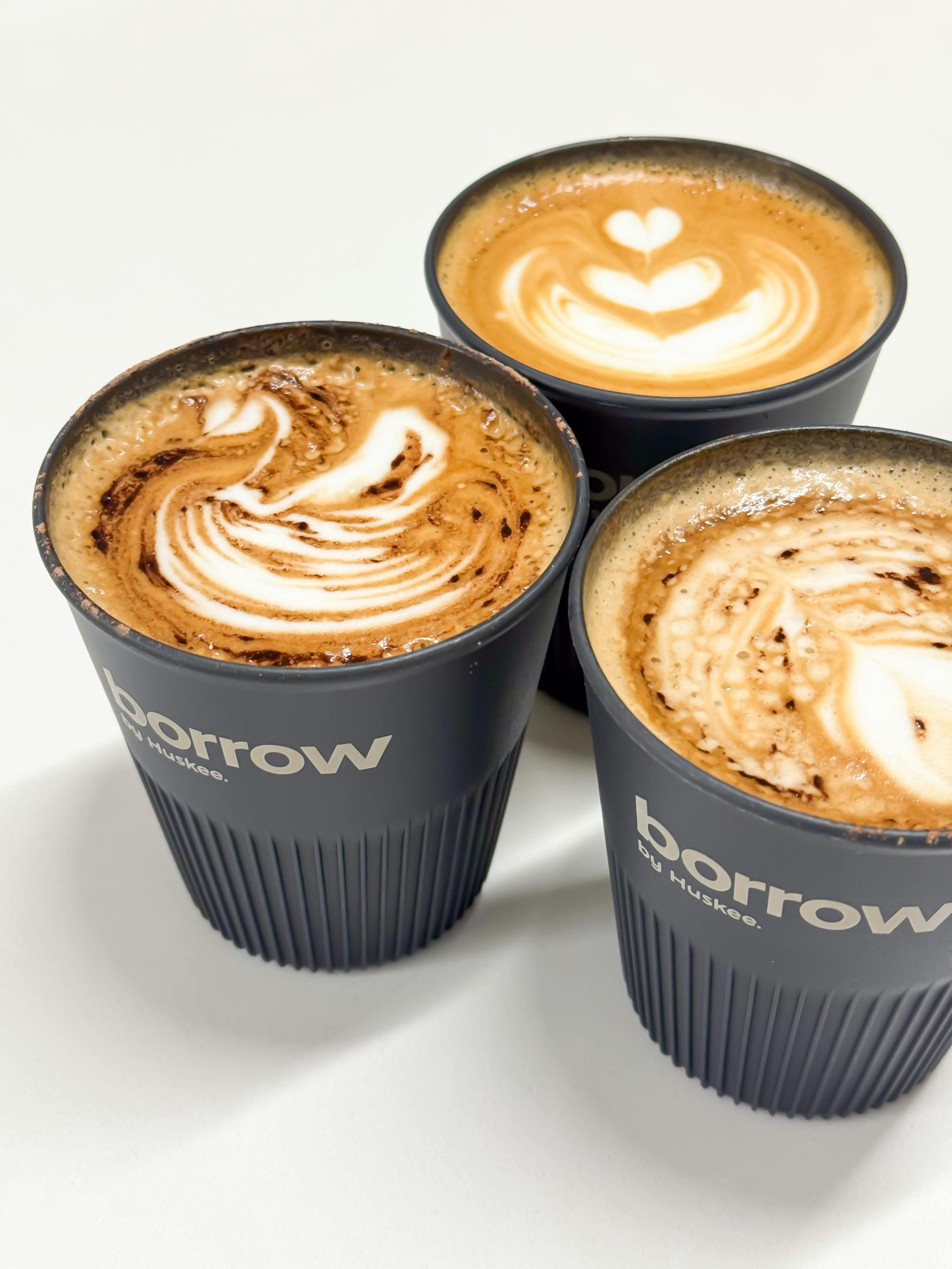Three beautiful Pure Bean coffees in Huskee Borrow cups with latte art, showcasing zero waste mantra