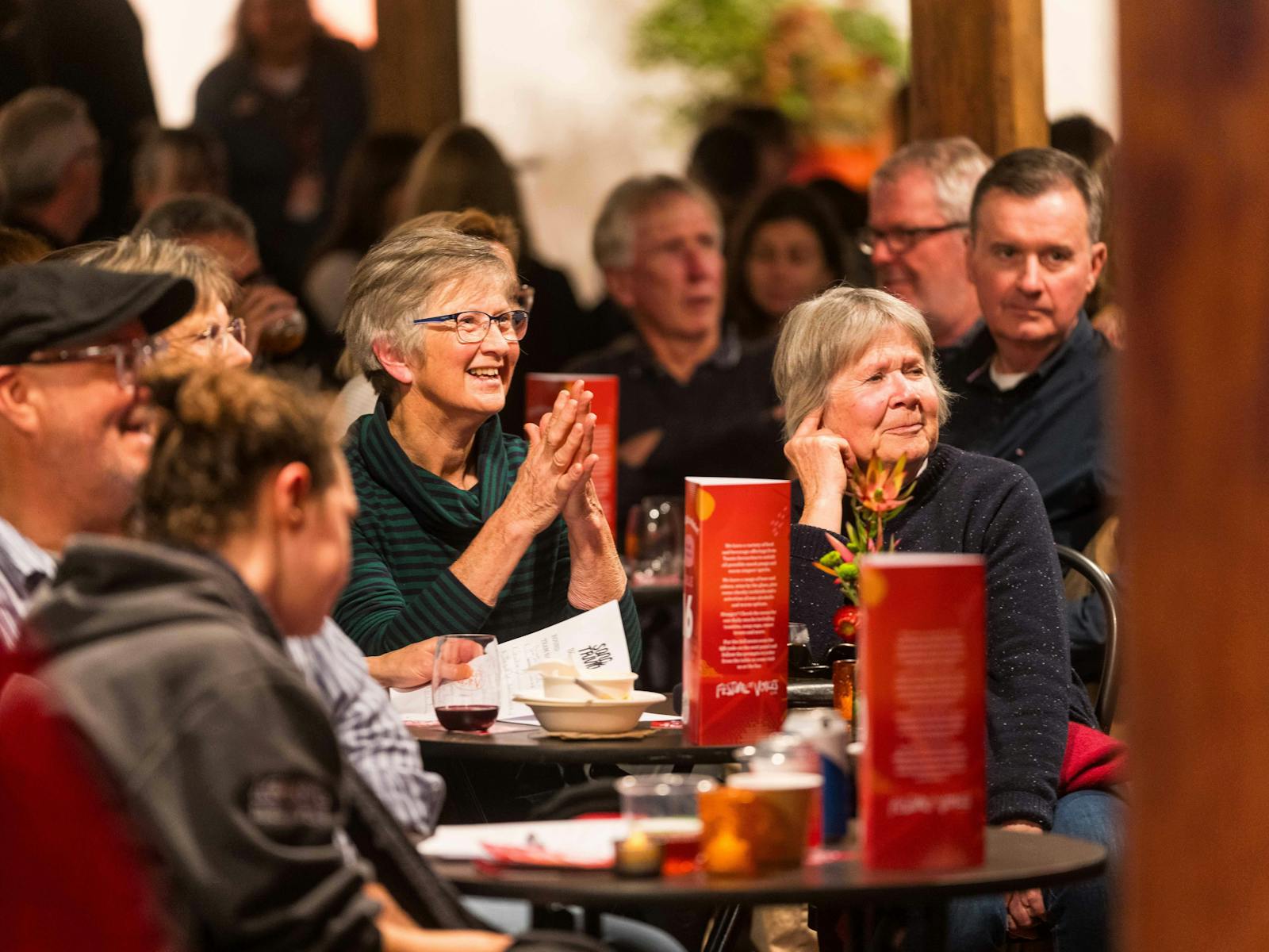 A colour photograph of people sitting at tables, smiling and laughing at a trivia night