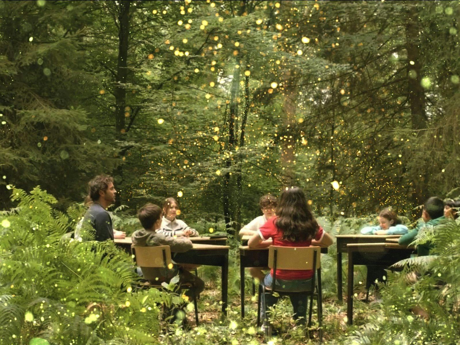 A group of children sitting at desks in a circle in the middle of a green forest