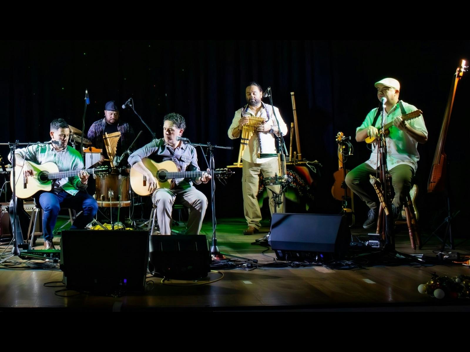 Five musicians perform live on stage, playing guitars, panpipes and percussion.
