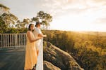 A man and a women looking out over the railing. Green grass and trees in the background.