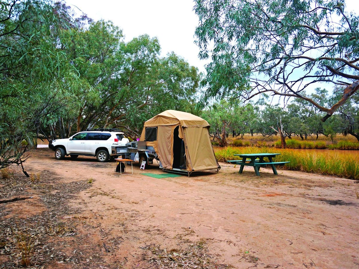 Four-wheel drive with camper trialer tent set up next to picnic table beside waterhole.