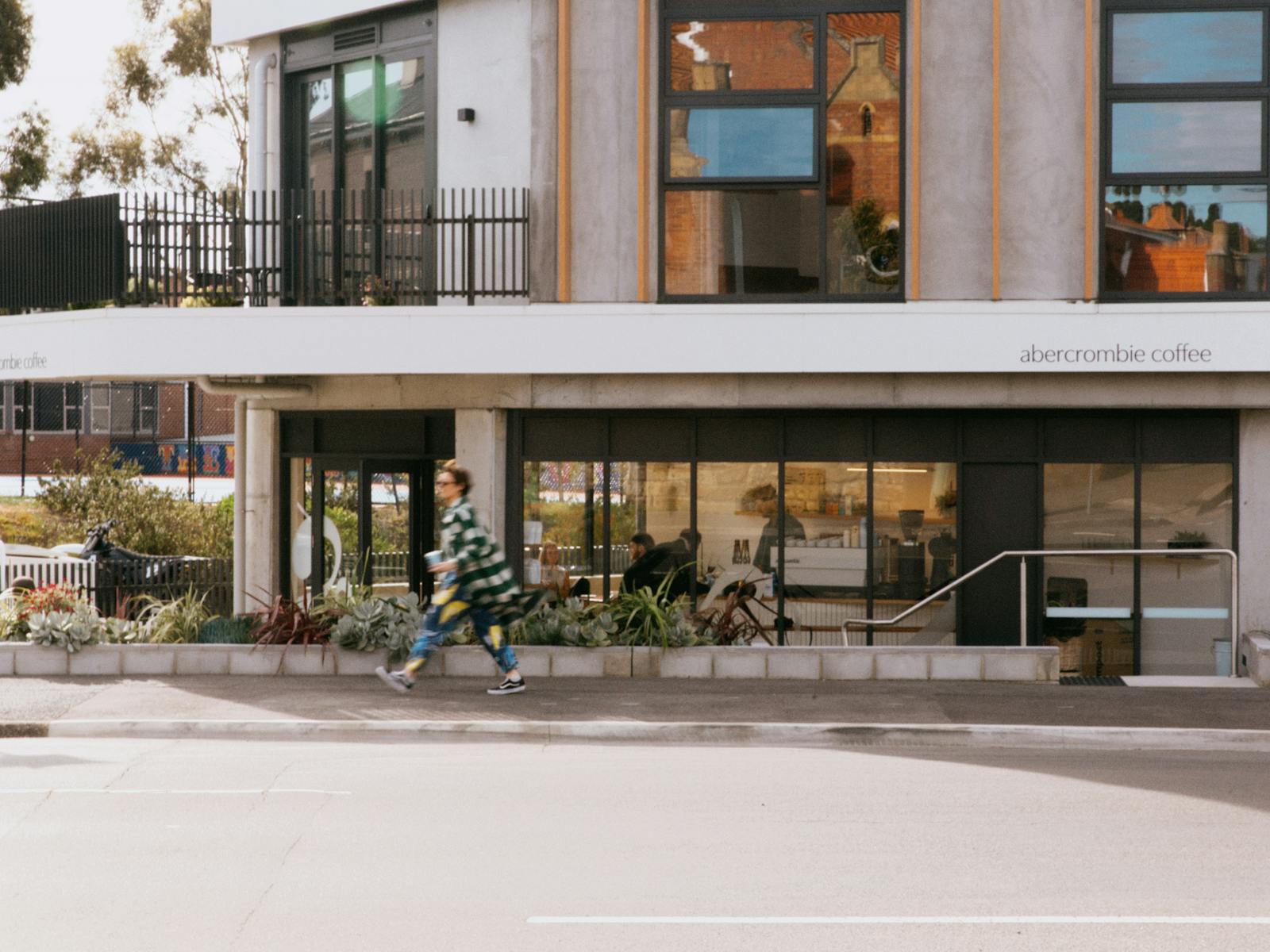 A woman in a flowing coat walks past coffee shop, Abercrombie Coffee, viewed from across a road.
