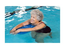 An older pretty lady with grey hair gently walking along the bottom of a blue pool on a blue board.