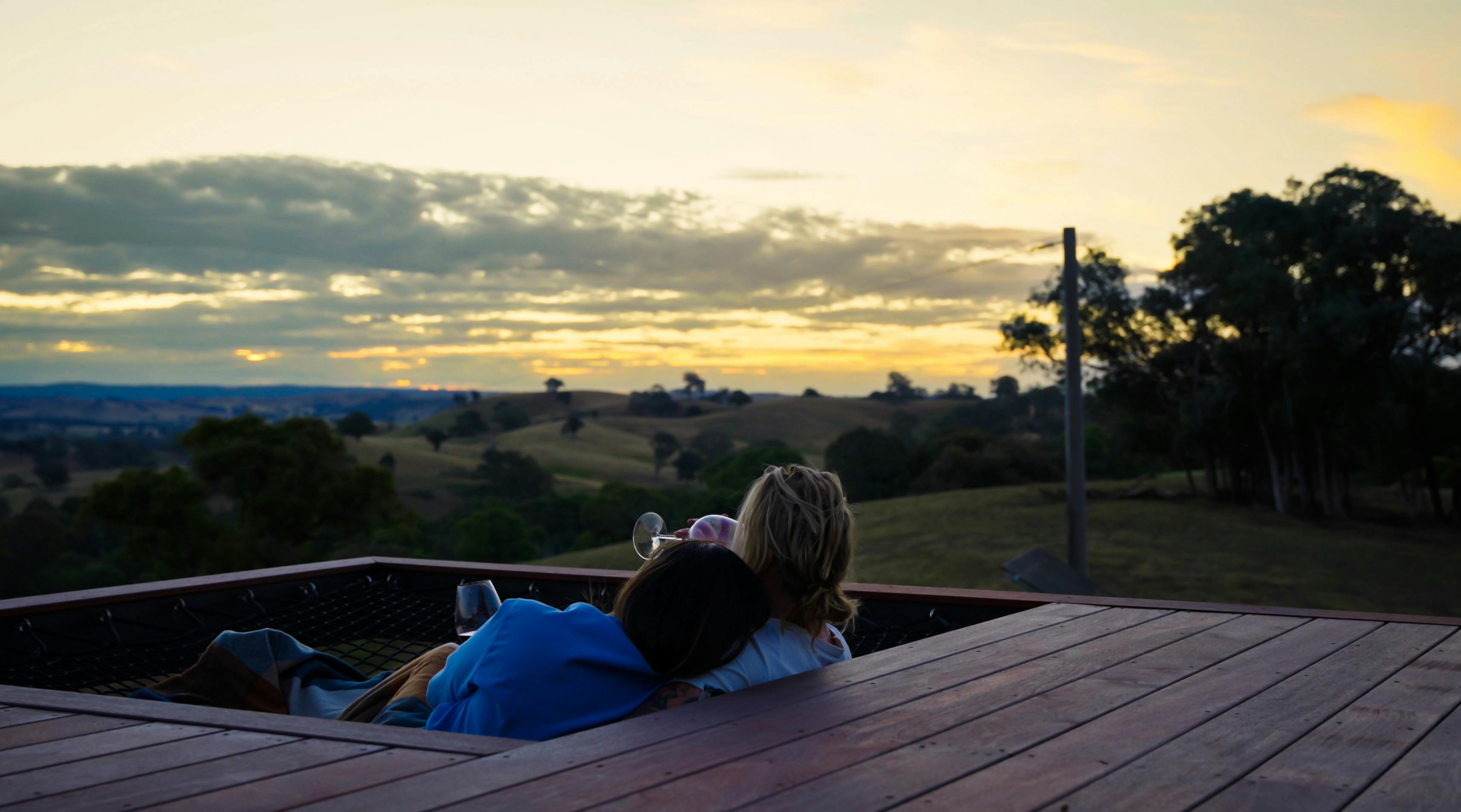 Couple embracing watching sun set in large hammock enjoying wine