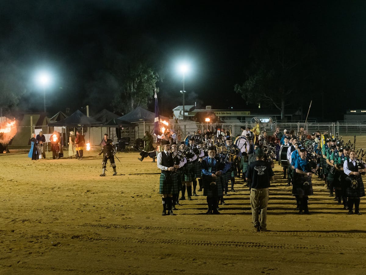 Pipers and drummers play on sandy arena, flanked by fire-breathing metal dragon and medieval knights