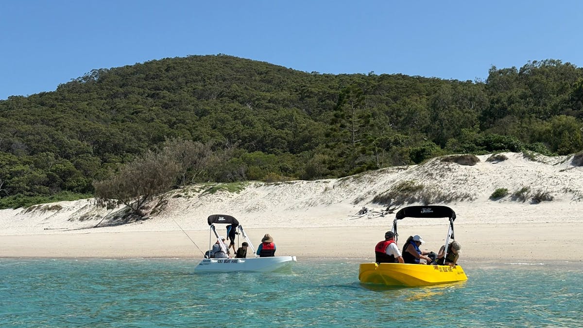 Two Polycraft hire boats near a sandy beach with guests onboard at Great Keppel Island.
