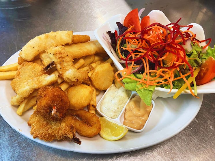 Variety of battered & crumbed & tempura seafood served on a plate with chips and salad