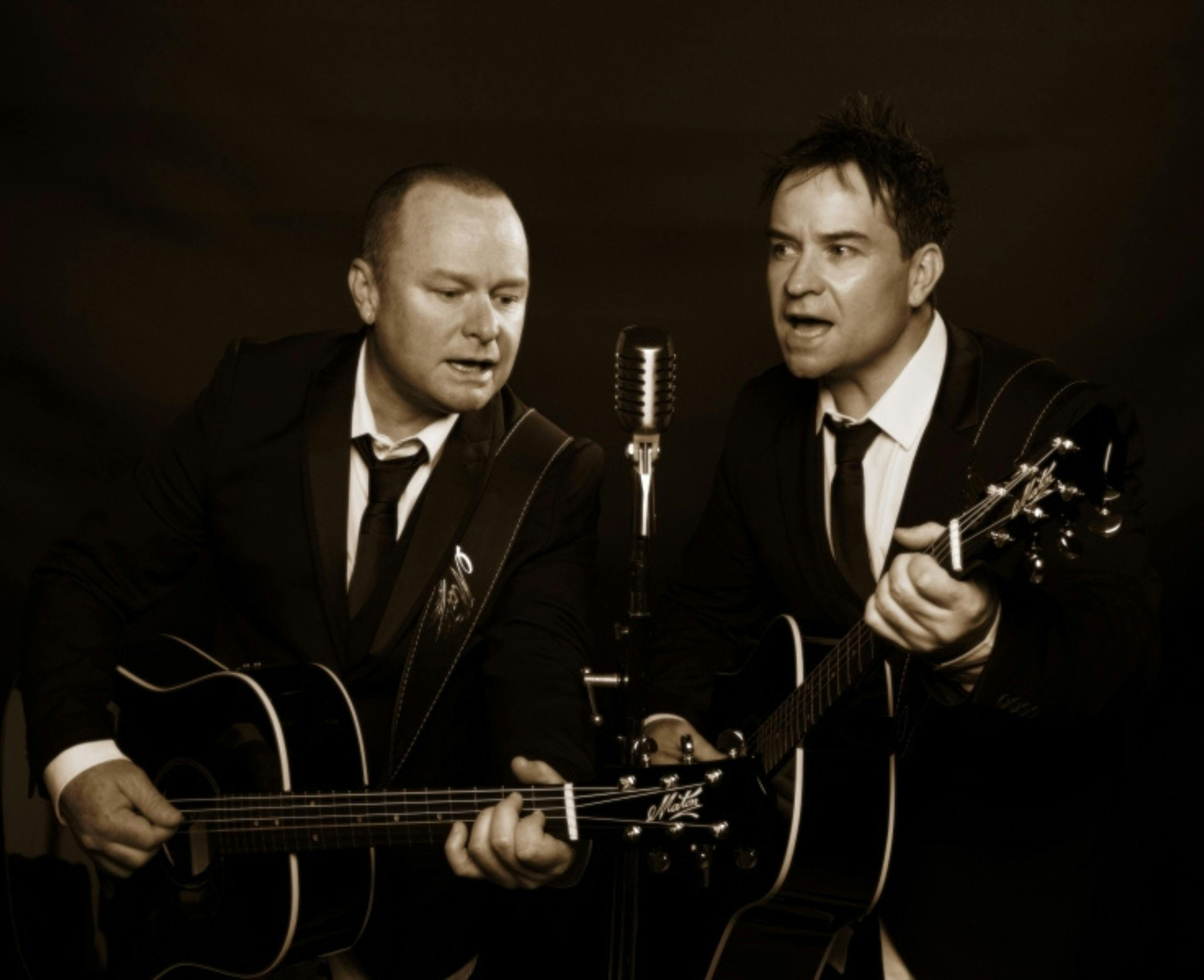 Two men playing guitars and singing into a microphone
