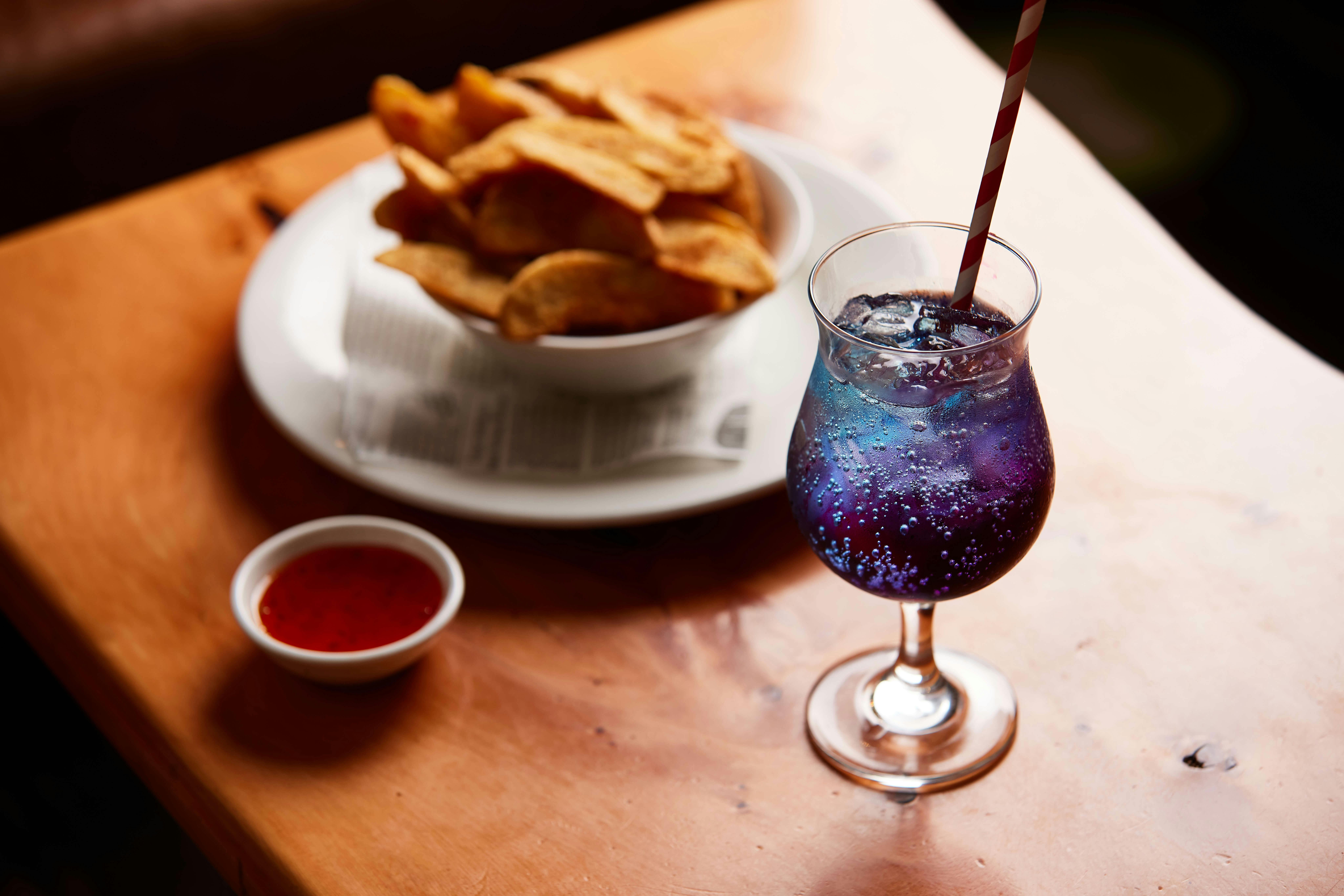 A blue cocktail sits in the foreground with a bowl of wedges