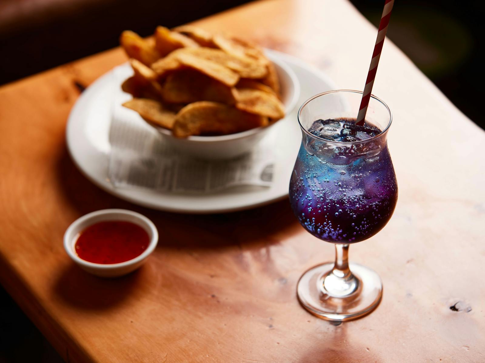 A blue cocktail sits in the foreground with a bowl of wedges