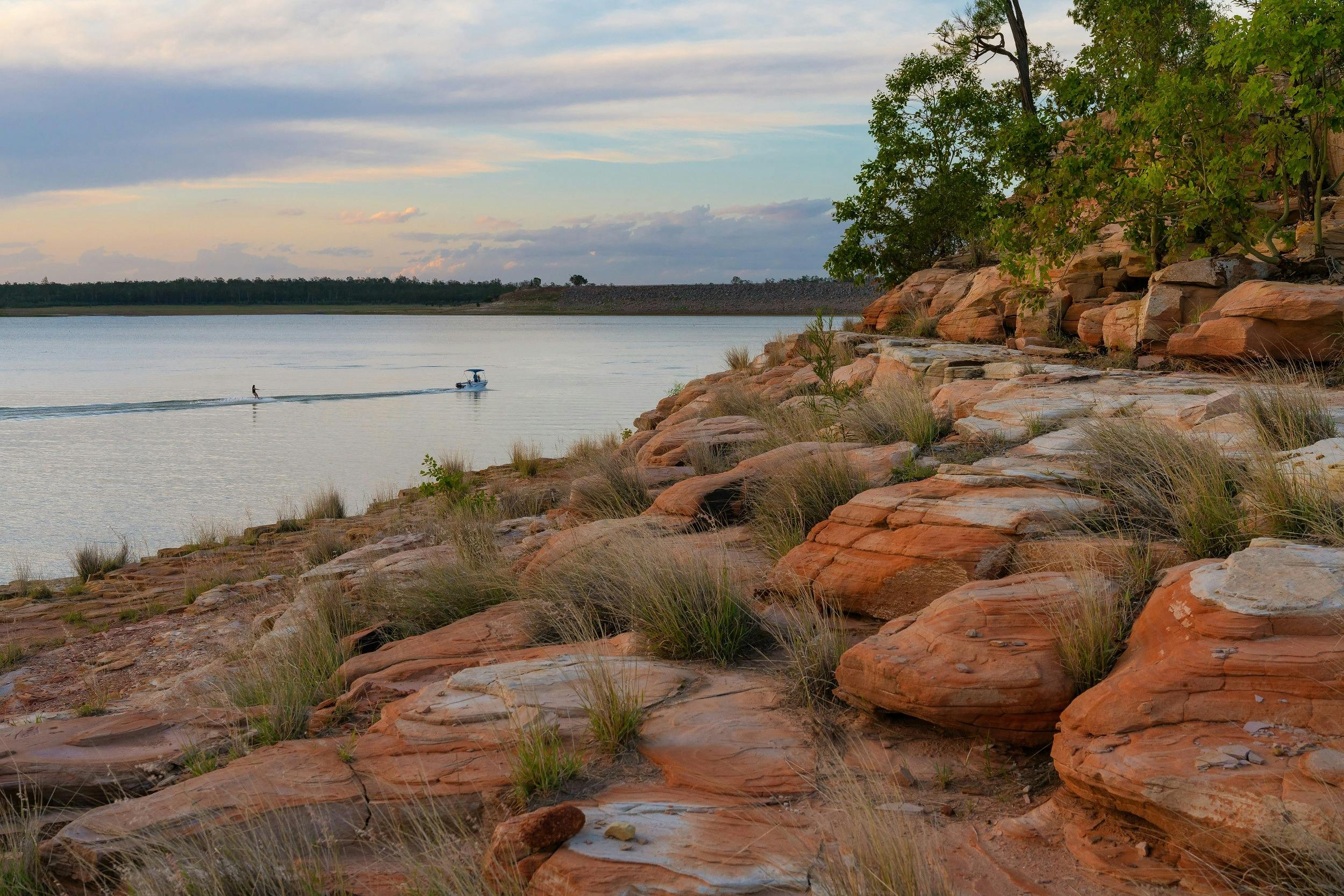 A rocky foreshore next to a large body of water,  with a small moving boat in far background