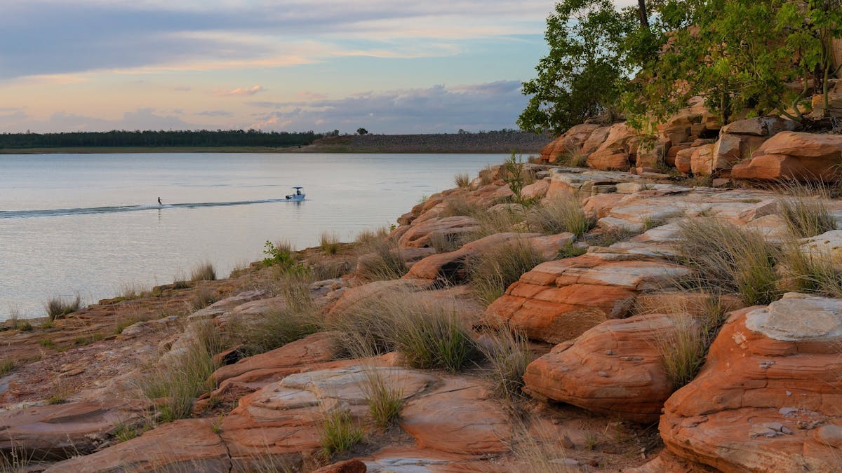 A rocky foreshore next to a large body of water,  with a small moving boat in far background