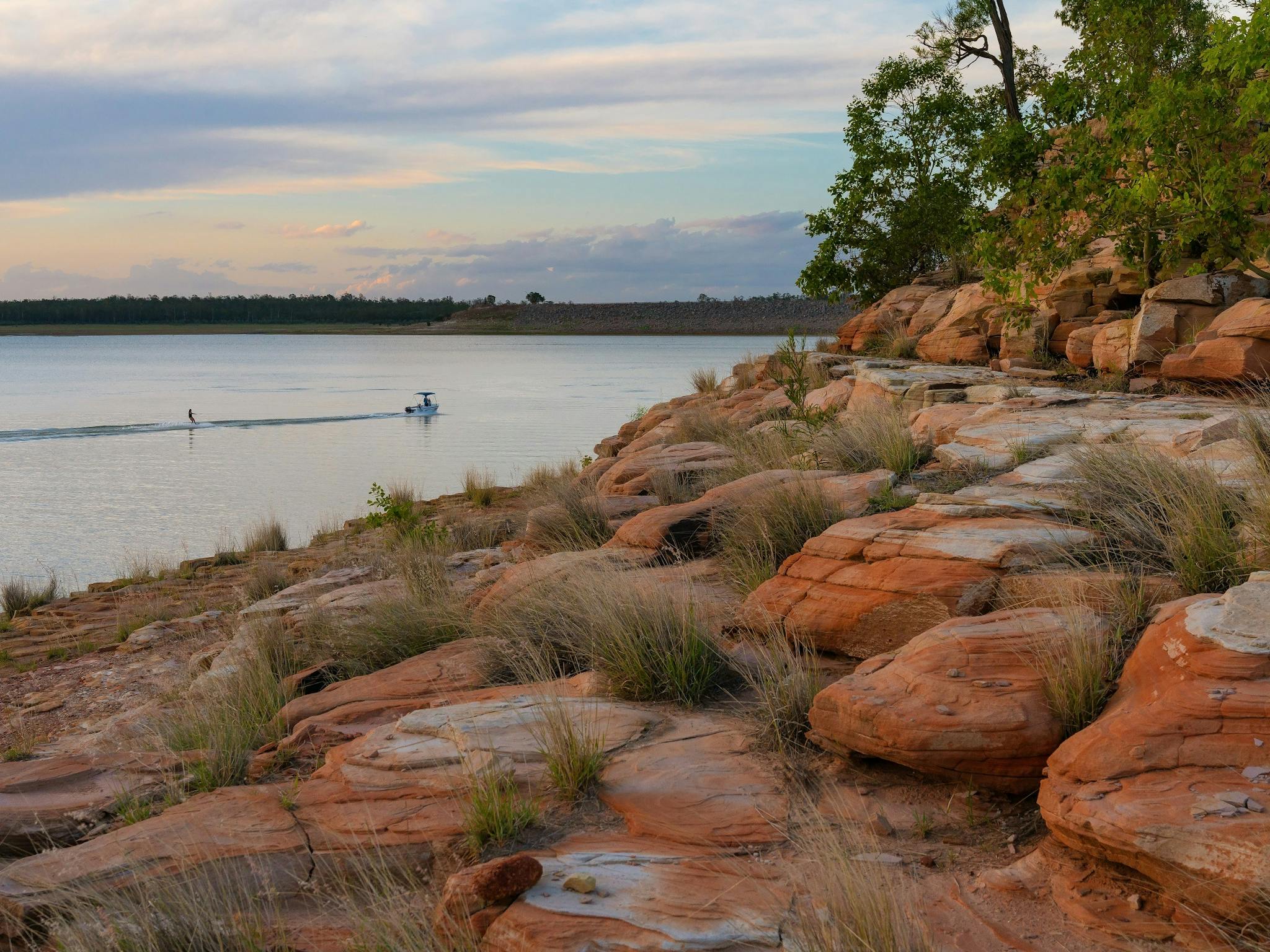 A rocky foreshore next to a large body of water, with a small moving boat in far background