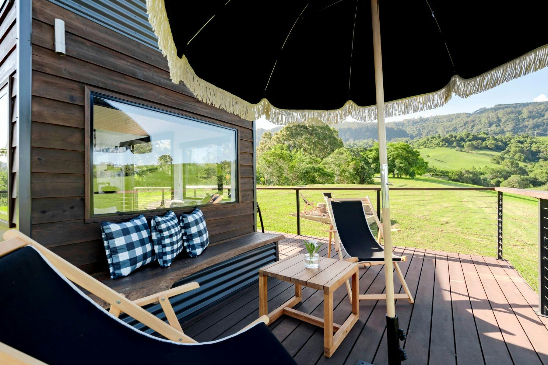 데크 구역의 이미지. 베개가 벤치에 깔끔하게 놓여 있는지 확인하세요. 우산은 그늘을 드리우기 위해 열려 있습니다.