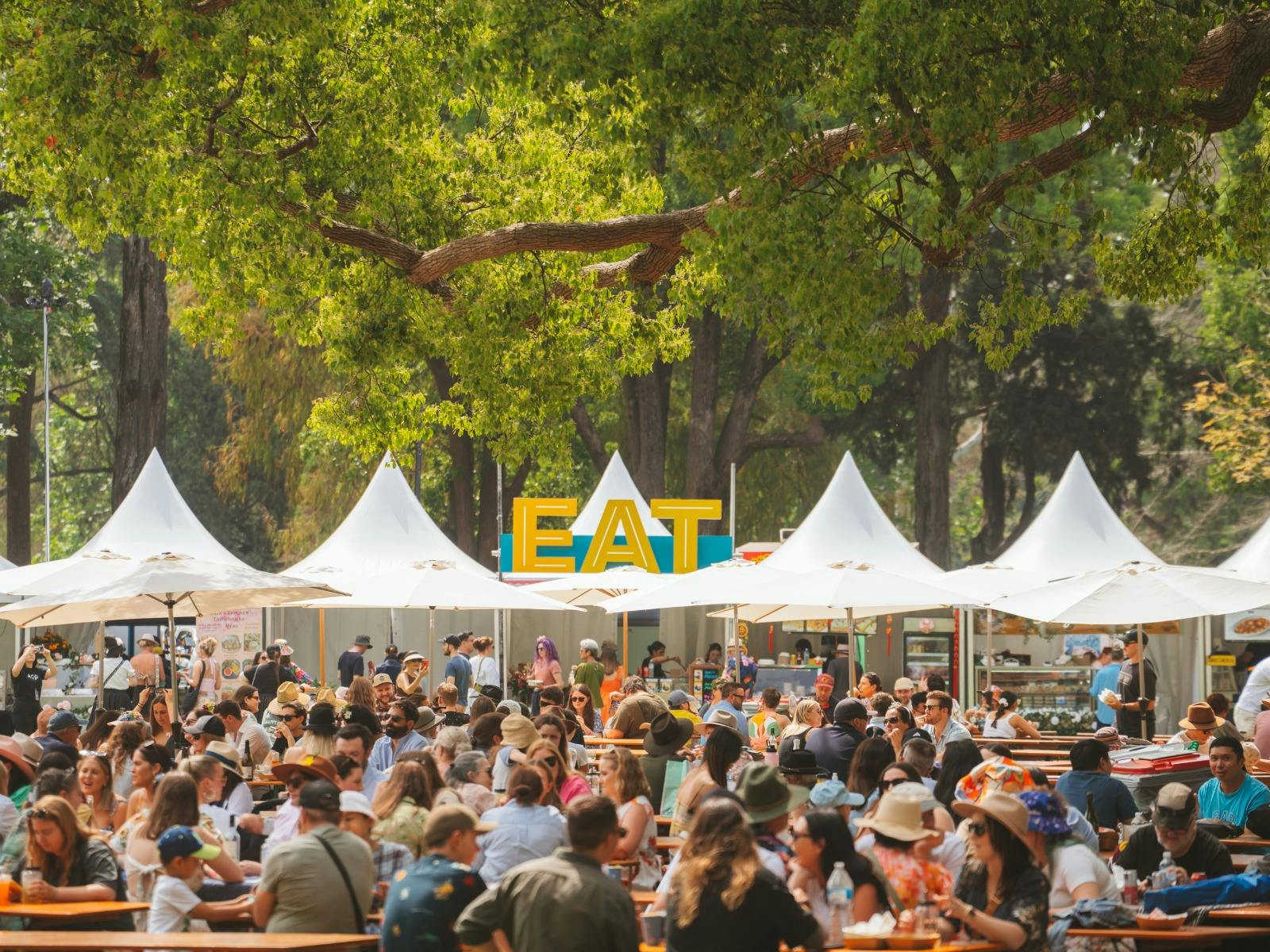A crowd of people at an outdoor food festival set in a leafy parkland. A crowd of people at an outdoor food festival set in a leafy parkland.