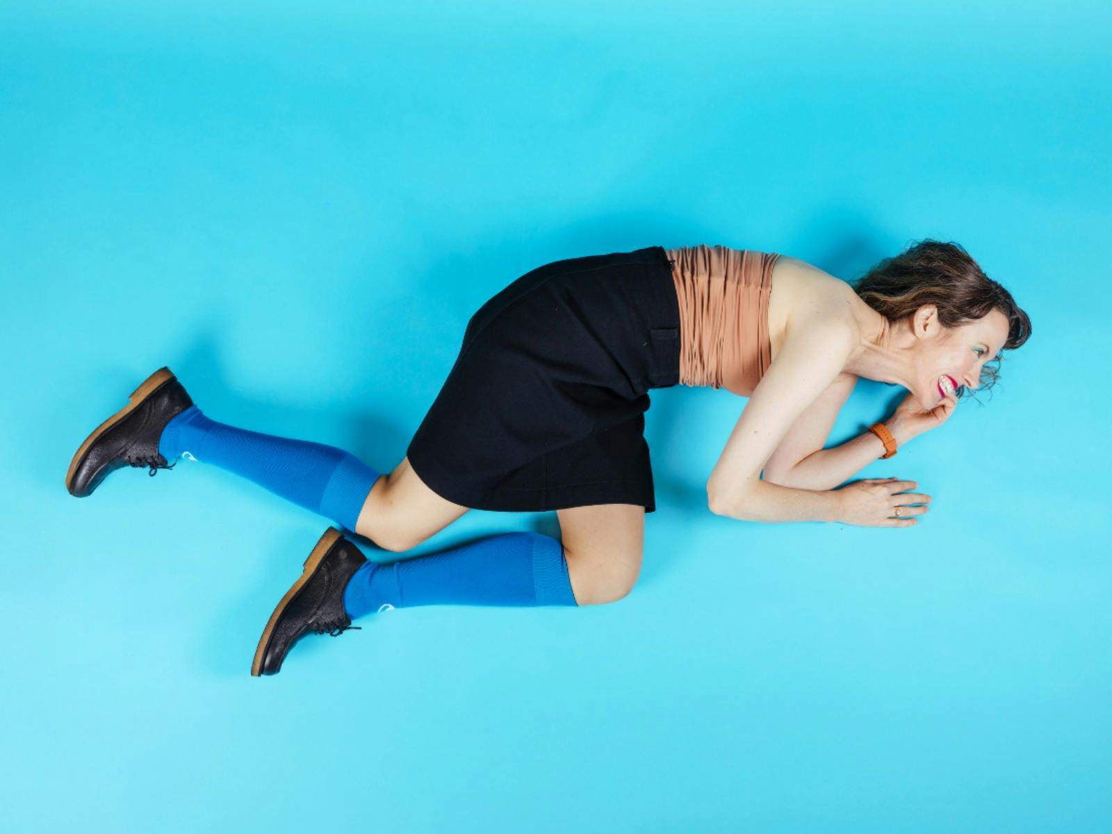 A woman smiles aggressively while lying down against a blue backdrop