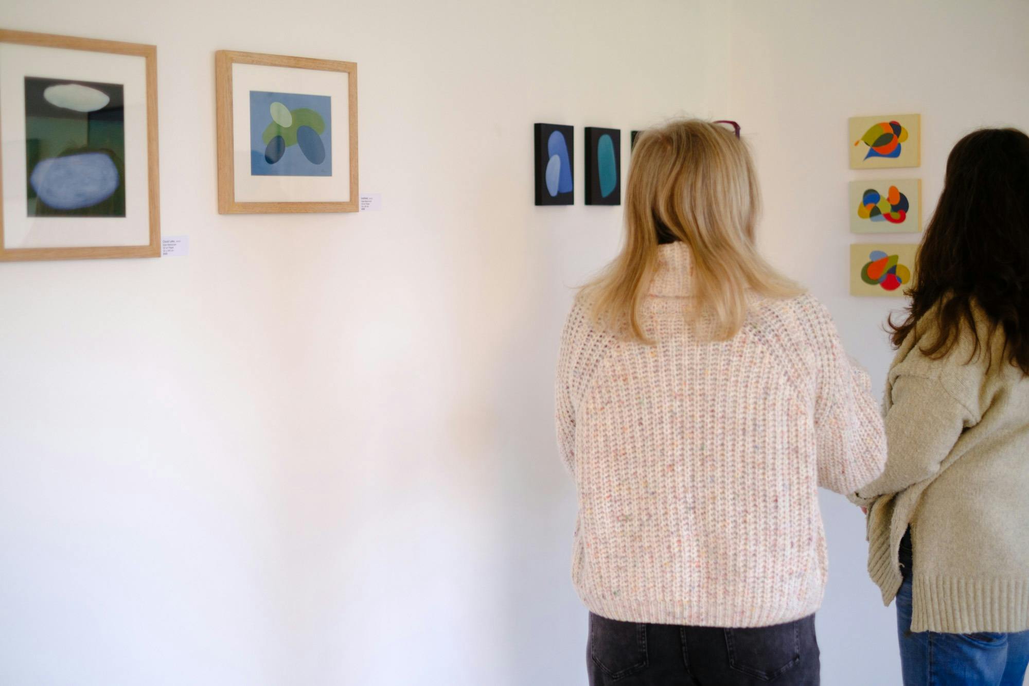 Two women in a gallery looking at paintings