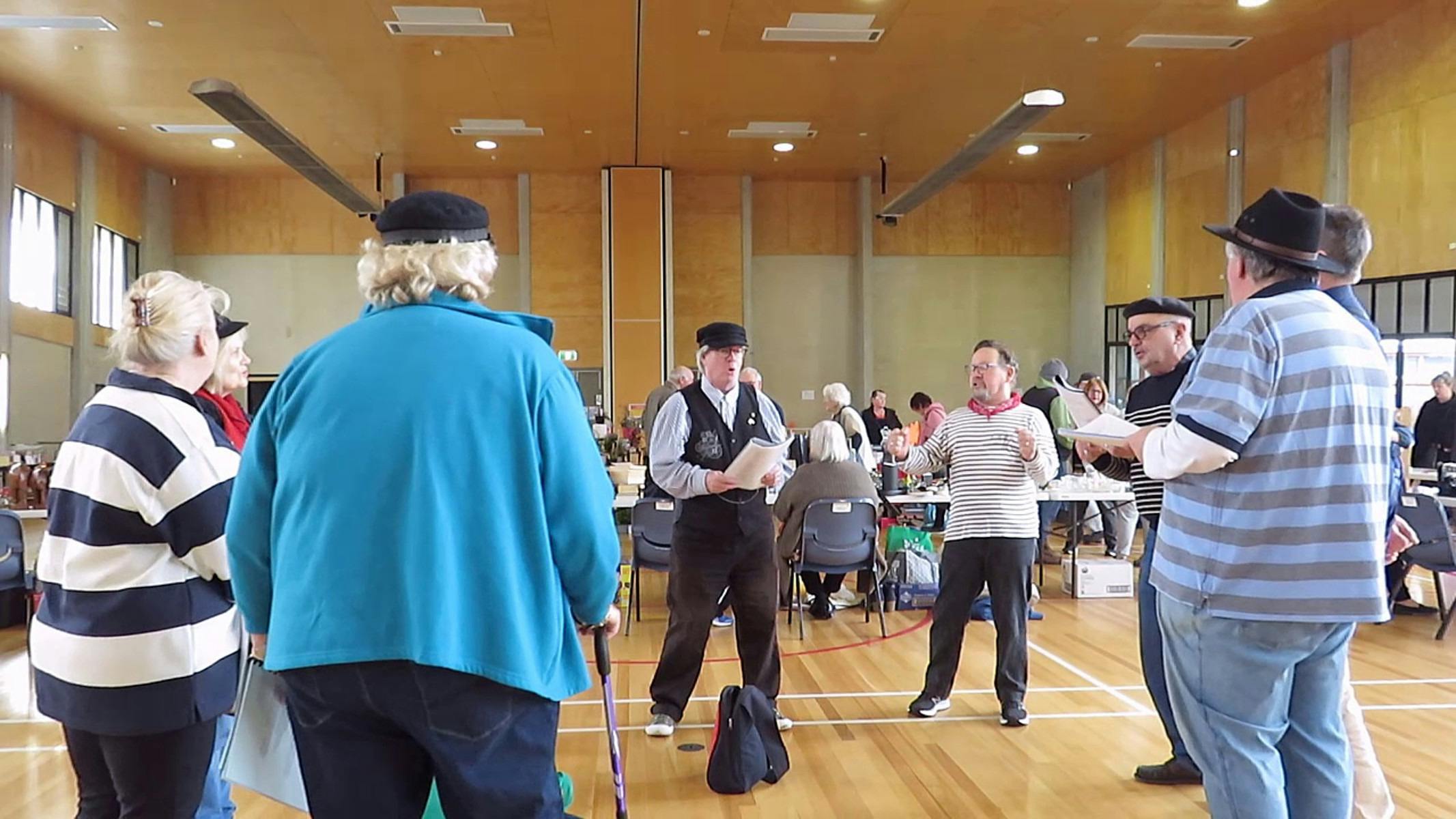 A group dressed in slightly nautical garb stand in a circle singing