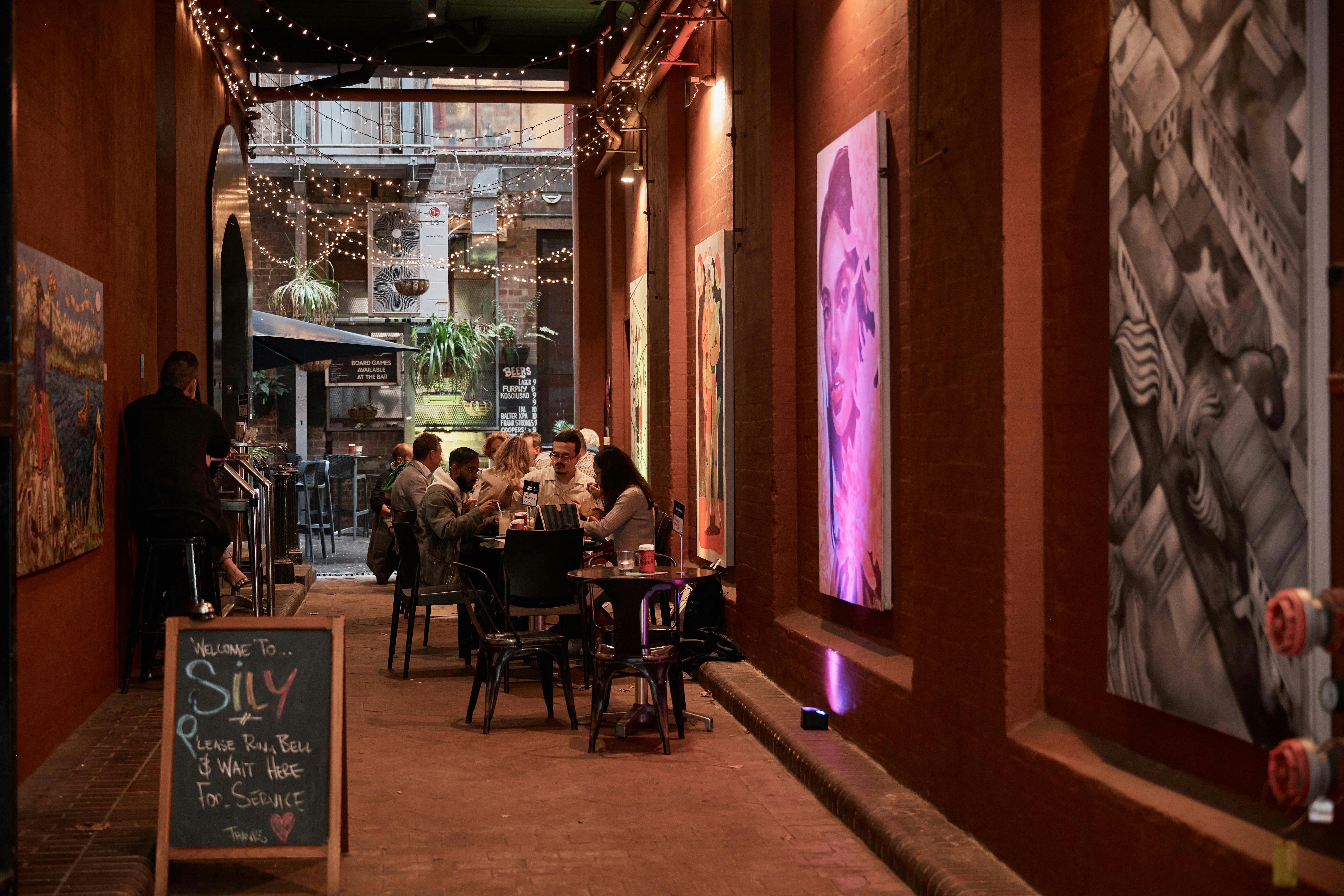 a carrieageway with people sitting at tables, and murals hanging on the walls.