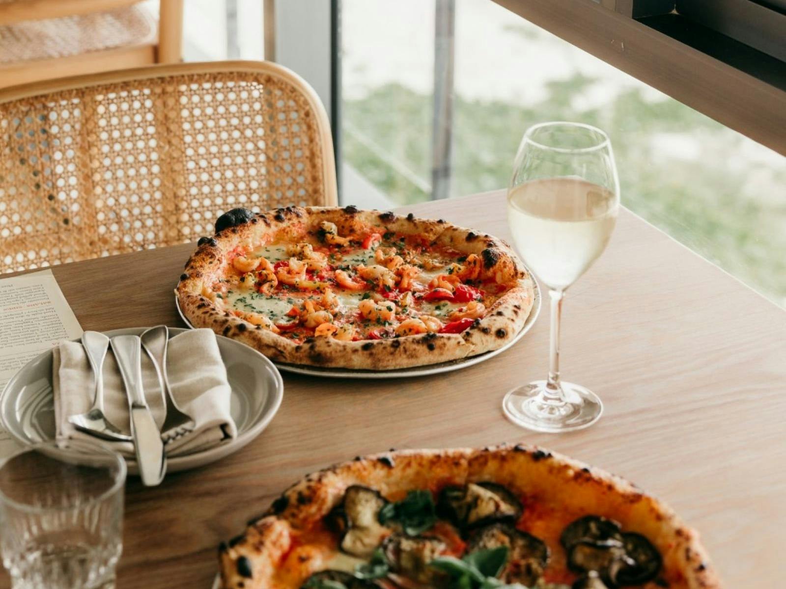 Two pizzas and wine glasses on timber table