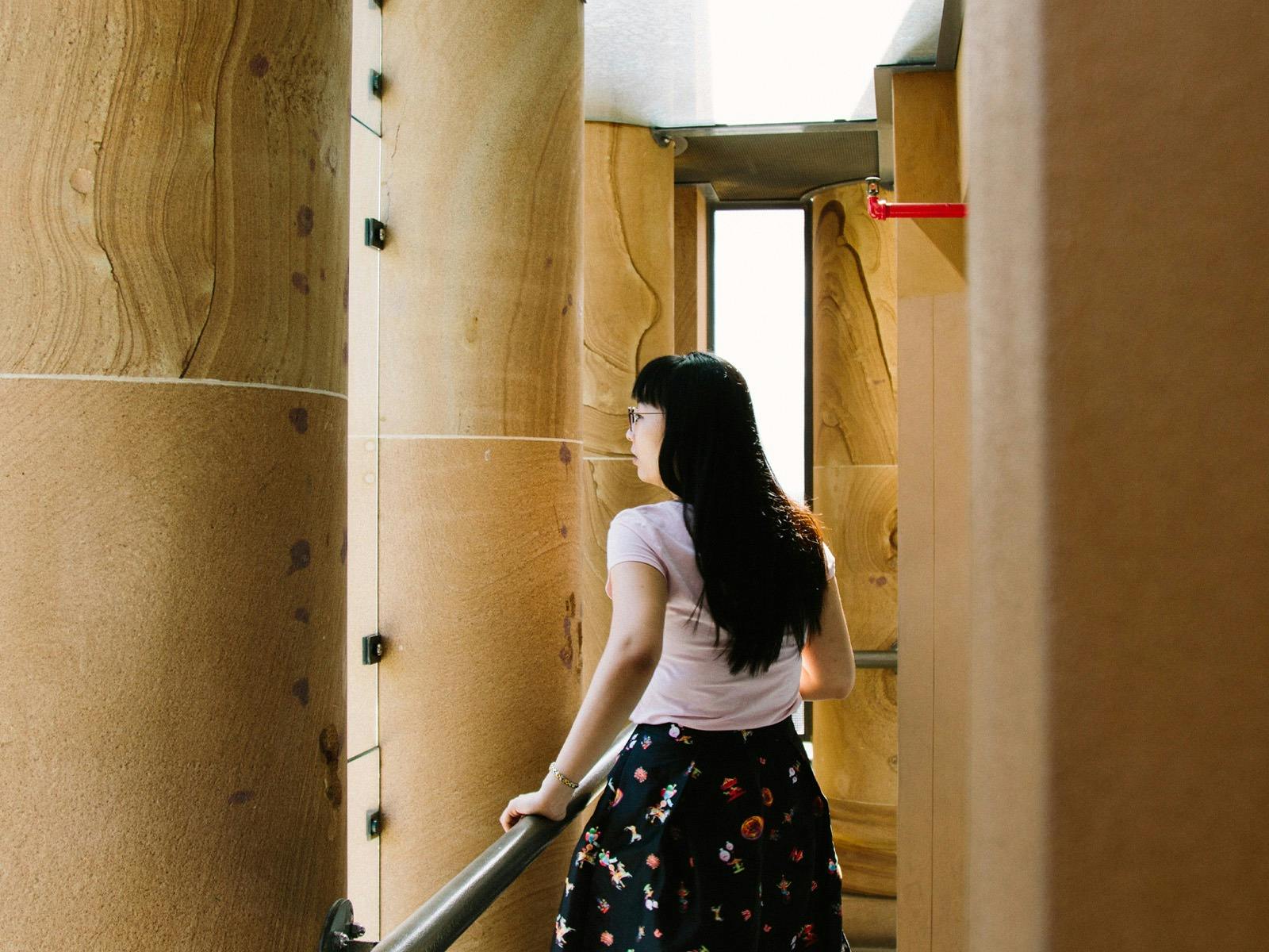 A person walks between large sandstone columns looking out between the columns.