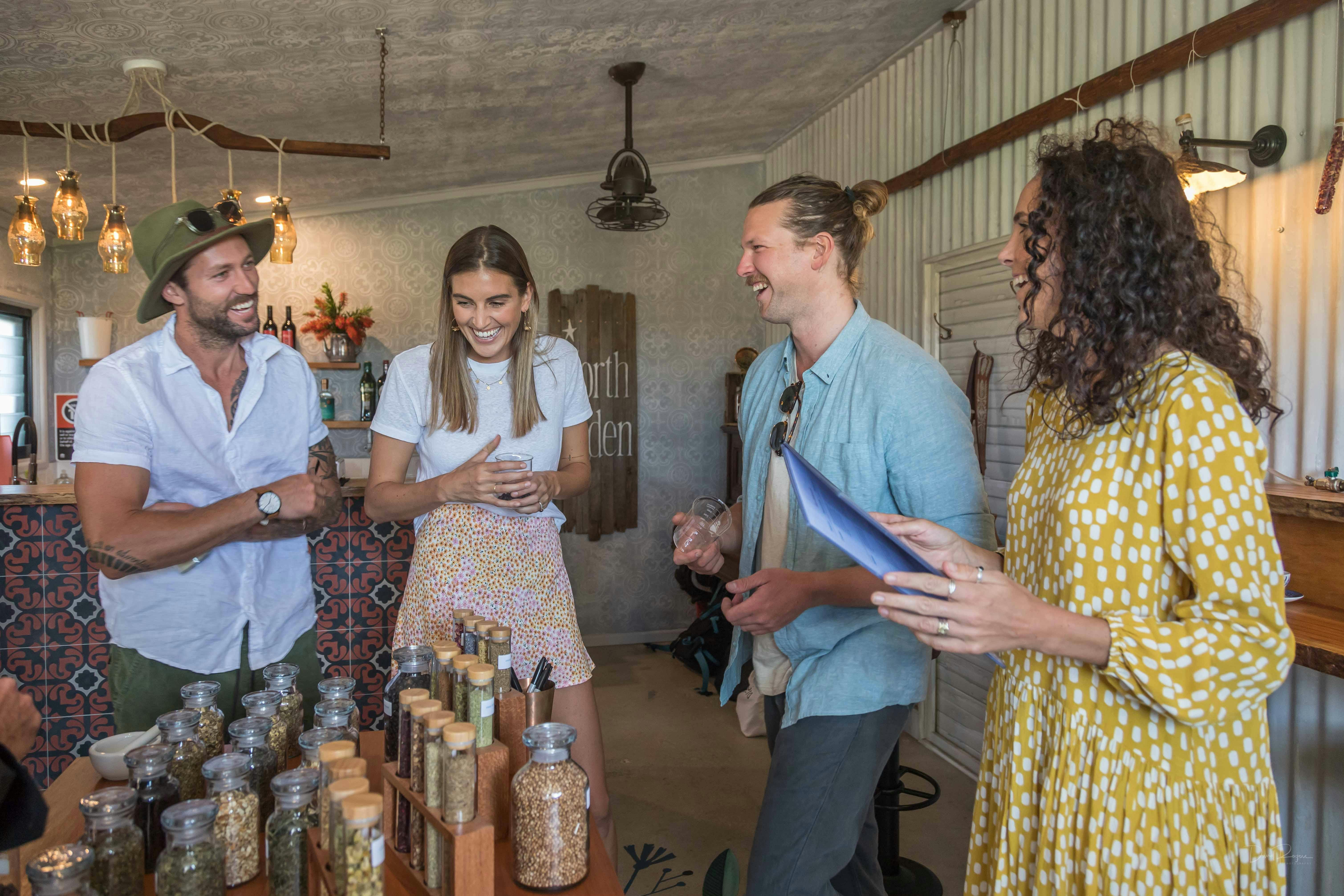 Four people laughing. Standing next to a table of glass jars filled with different botanicals.