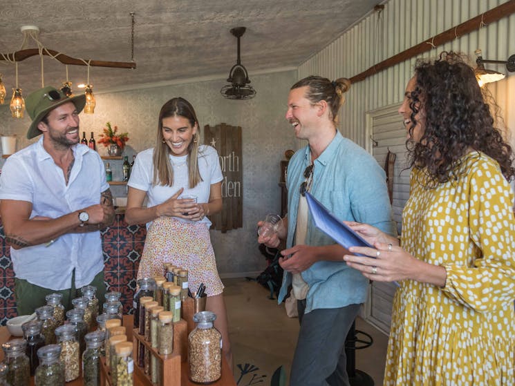 Four people laughing. Standing next to a table of glass jars filled with different botanicals.