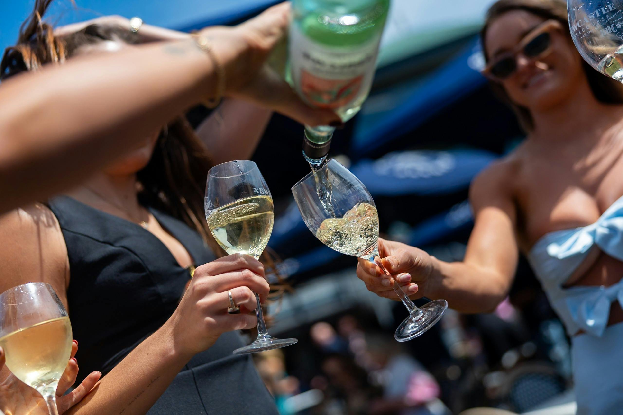 People holding wine glasses while pouring wine outdoors at Newcastle Racecourse.