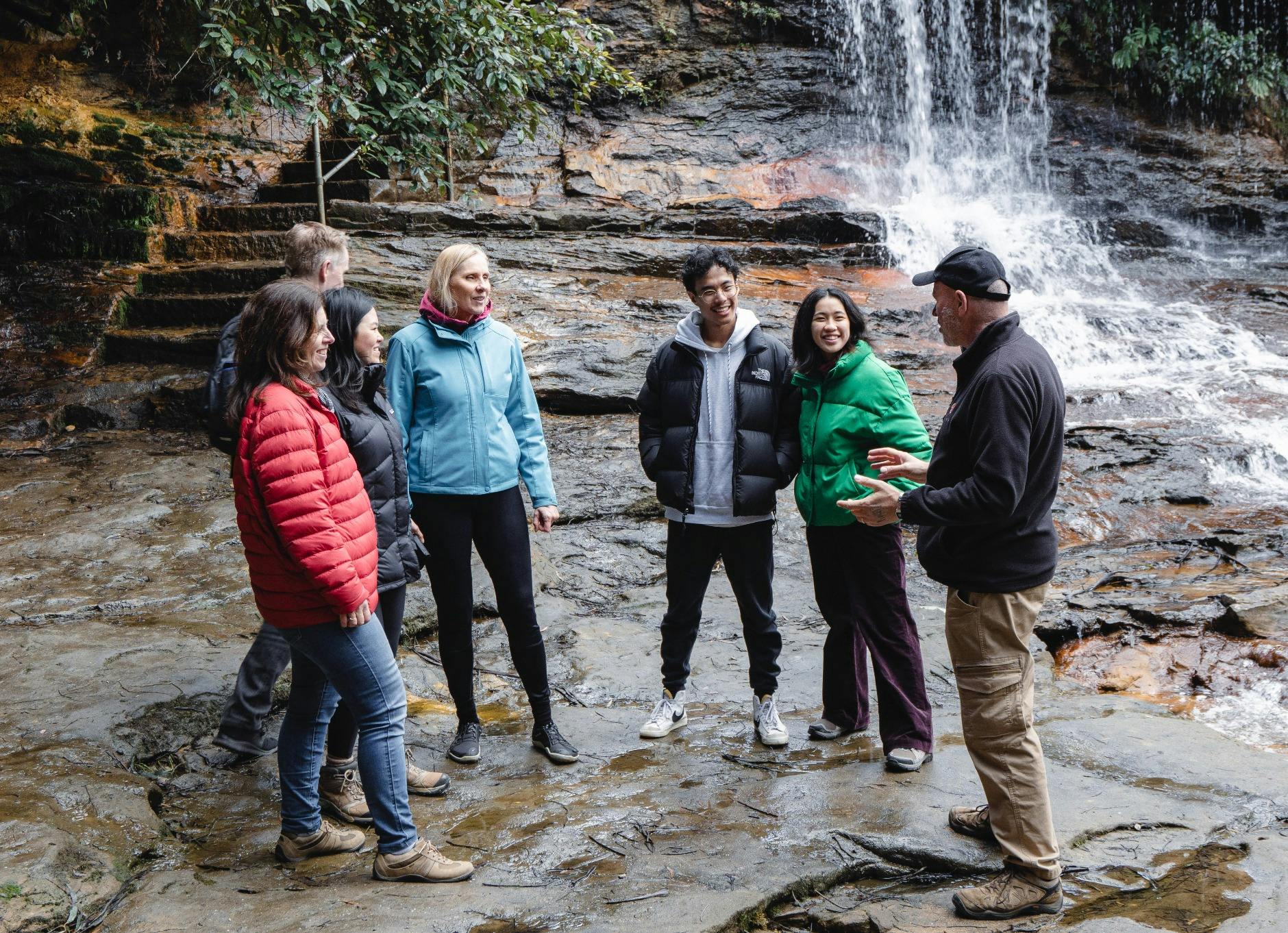 Tour group standing at base of Wentworth Falls waterfall in Blue Mountains with guide