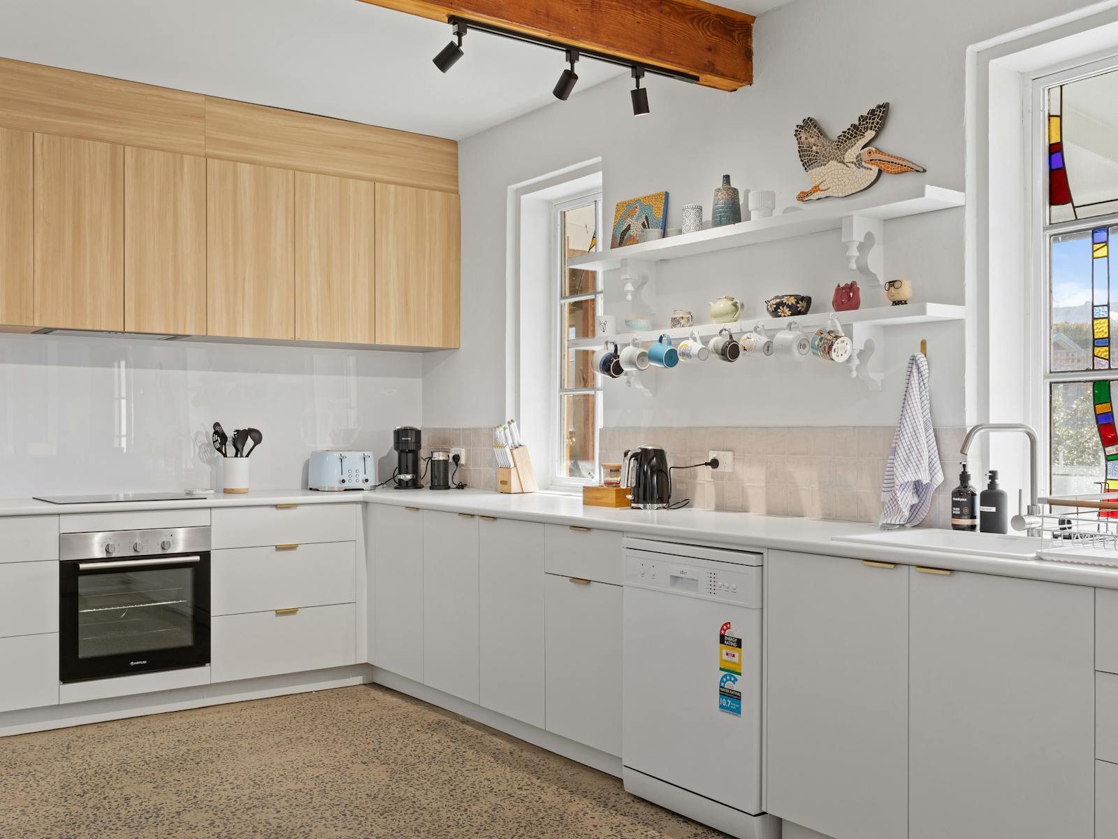 Kitchen with oven, sink, appliances, shelving with mugs, and stained glass windows