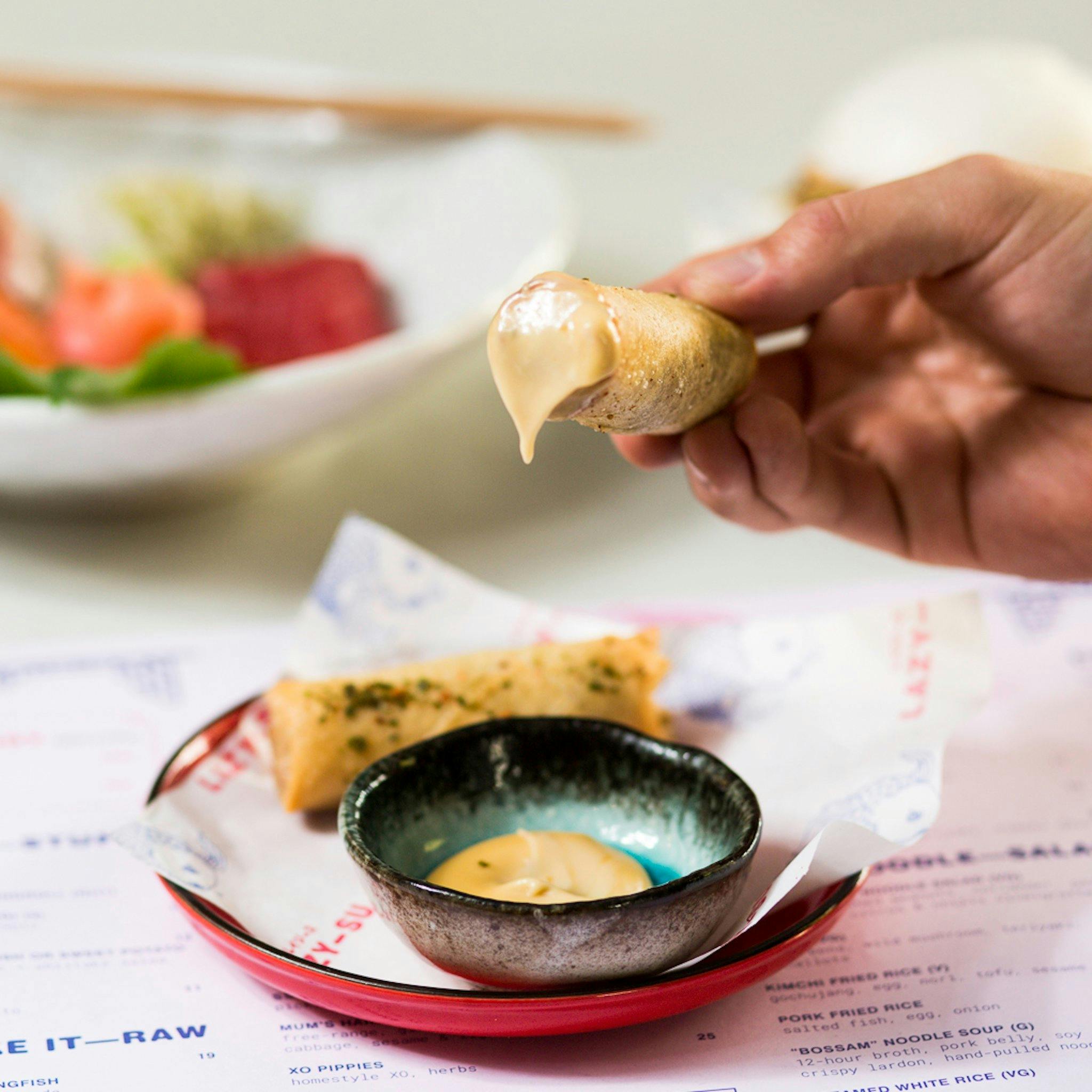 Hand holding a spring roll dipped in sauce