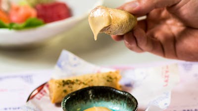 Hand holding a spring roll dipped in sauce