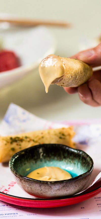 Hand holding a spring roll dipped in sauce
