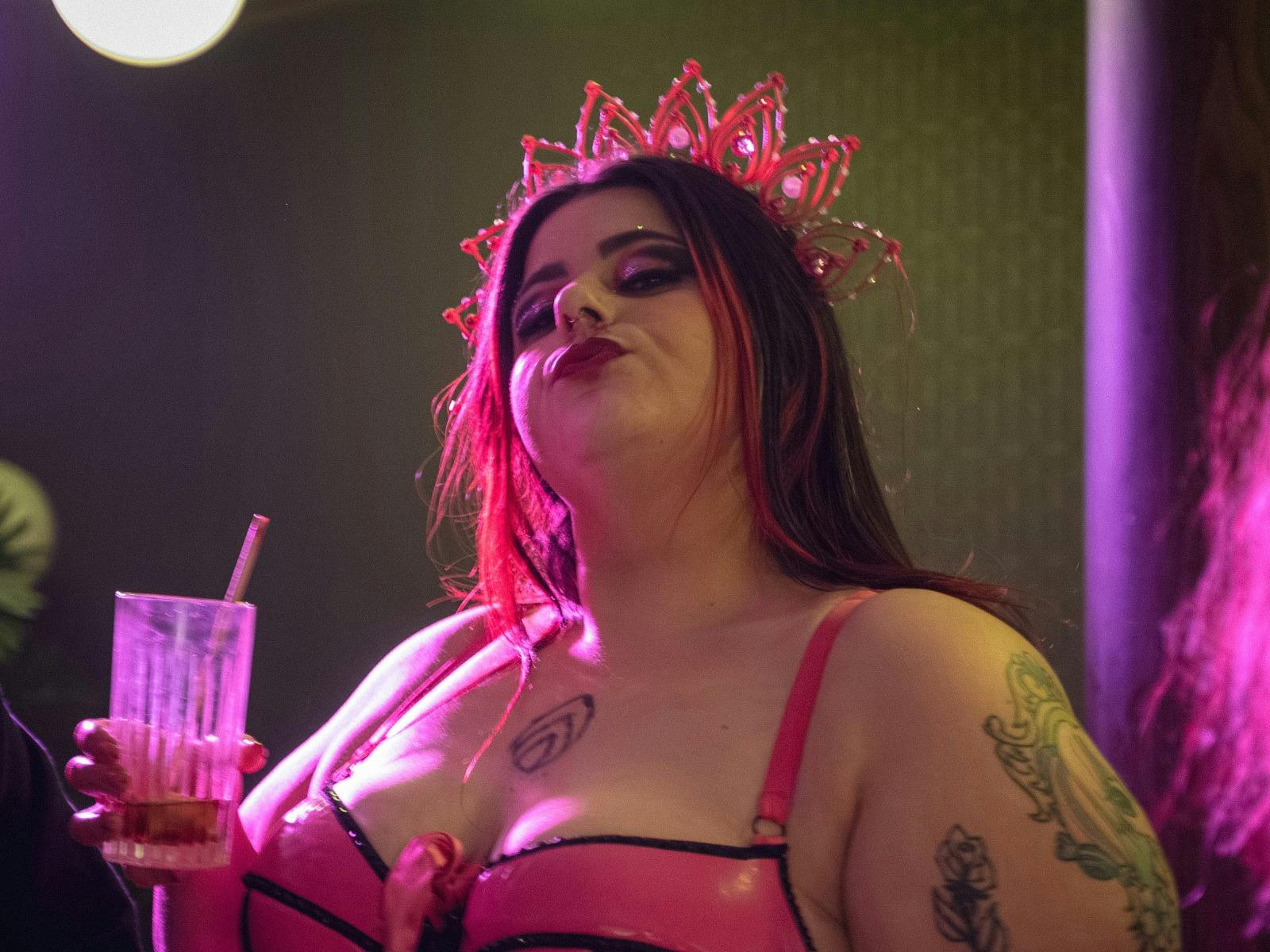 A plus sized white performer in a pink crown looks down at camera