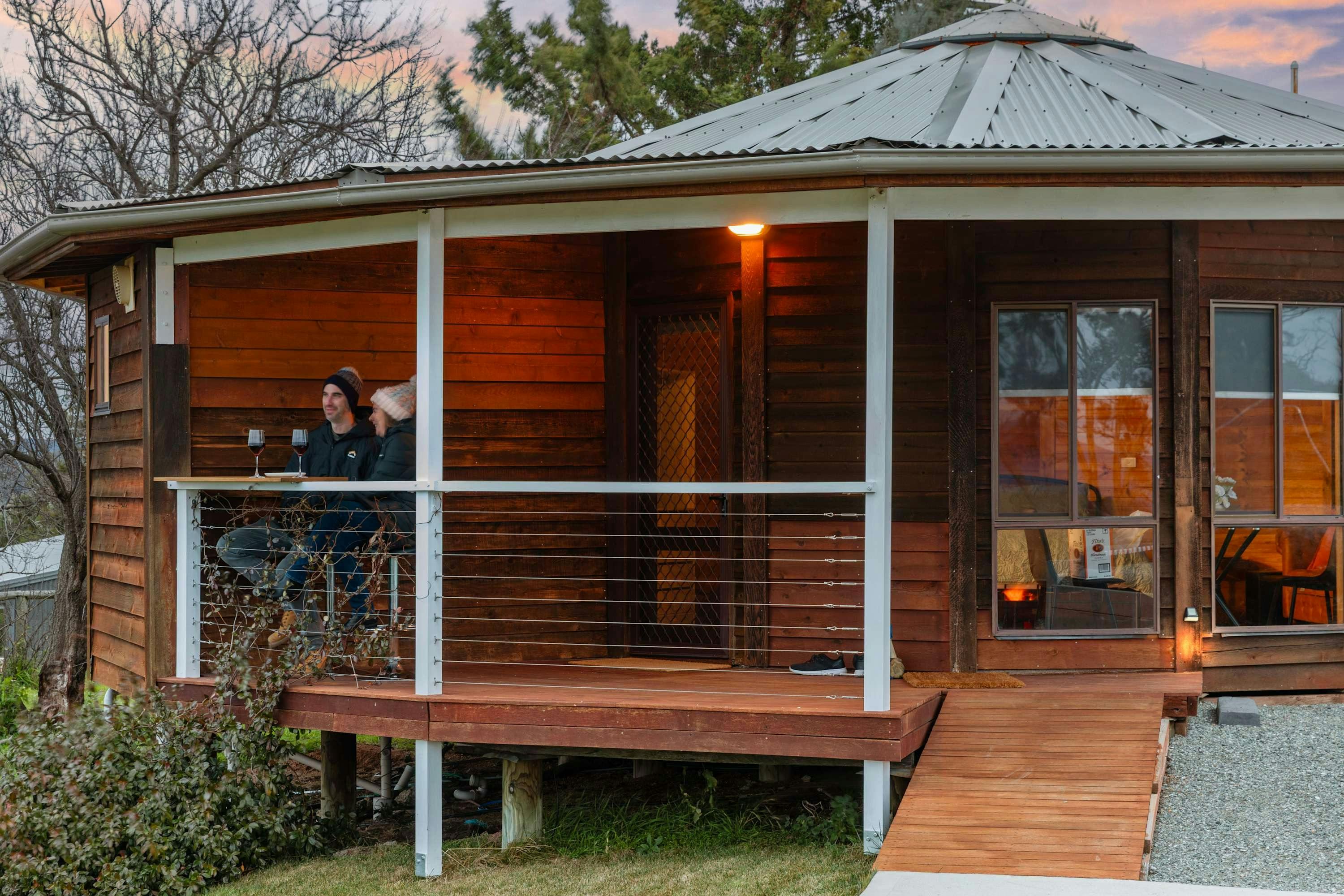 Exterior of the yurt on the hill with a couple on the deck enjoying a wine at sunset