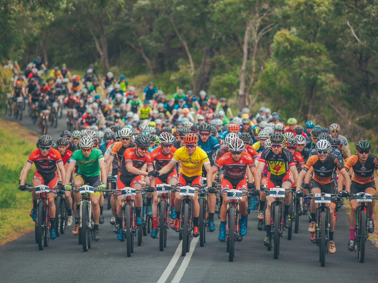Mass group of mountain bike riders racing on bitumen road