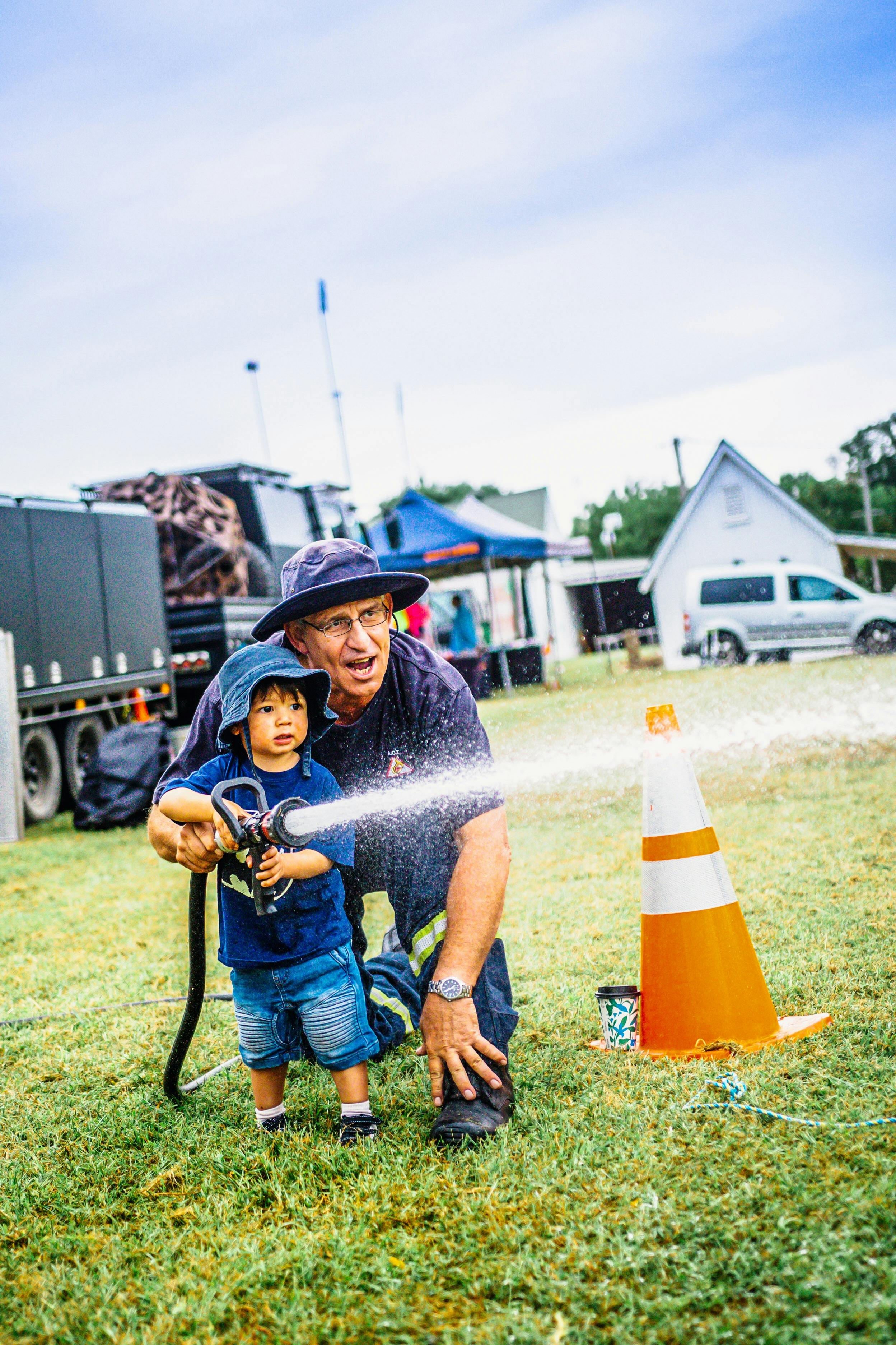 Rural fire service volunteer helping a small child use fire hose at Harvest Day Out