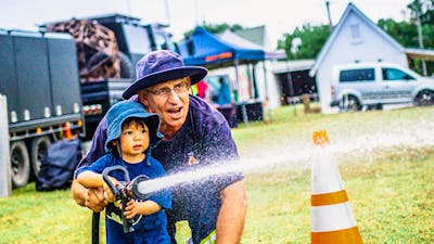 Rural fire service volunteer helping a small child use fire hose at Harvest Day Out